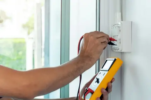 Elektryk wykonuje pomiar impedancji pętli zwarcia za pomocą żółtego miernika.