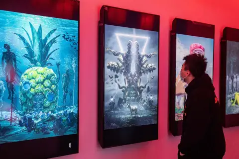 Ein Mann betrachtet digitale Kunstwerke, die an einer Wand hängen. Die Werke zeigen surreale Szenen, wie eine Ananas unter Wasser mit Skeletten und eine symmetrische Figur mit vielen Armen. Diese Werke stammen von einem berühmten Grafik Künstler.