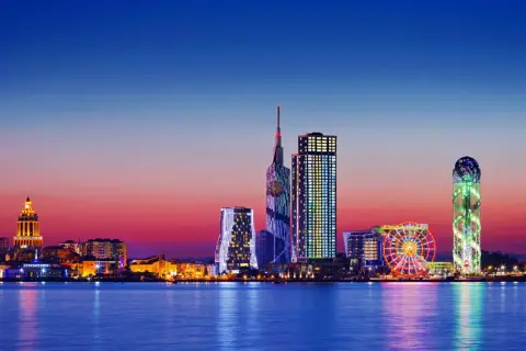 Widok na nowoczesną panoramę Batumi, stolicę Adżarii, o zachodzie słońca. Błyszczące wieżowce i diabelski młyn odbijają się w spokojnej wodzie.