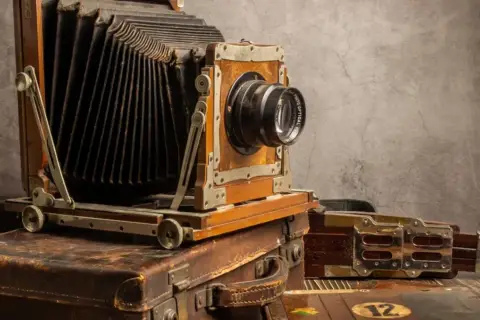 Antyczny aparat mieszkowy na kufrach. Zastanawiasz się, w którym roku wynaleziono aparat fotograficzny?