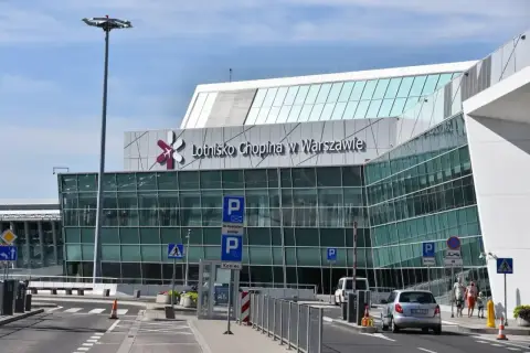 Nowoczesny budynek Lotniska Chopina w Warszawie z charakterystycznym logo. Samochody podjeżdżają do terminala.