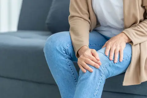 Frau sitzt auf Sofa, hält ihr Knie. Sie spürt ein unangenehmes Kribbeln in den Beinen.
