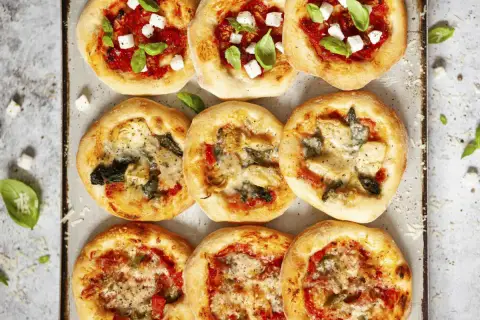 Mini pizze z ciasta na pizzę, niektóre z serem i bazylią, inne z warzywami.