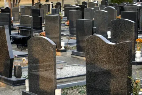 Nagrobki na cmentarzu, gdzie można wykupić miejsca na cmentarzu za życia. Widać ławki i kwiaty.
