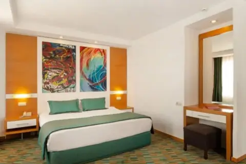 Pokój w Ladonia Hotels Adakule: łóżko z zieloną pościelą, kolorowe obrazy nad wezgłowiem, toaletka z lustrem.