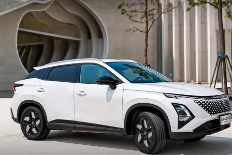 Biały OMODA hybryda zaparkowany przed nowoczesnym budynkiem. Stylowy SUV z charakterystycznym grillem i dynamiczną linią nadwozia.
