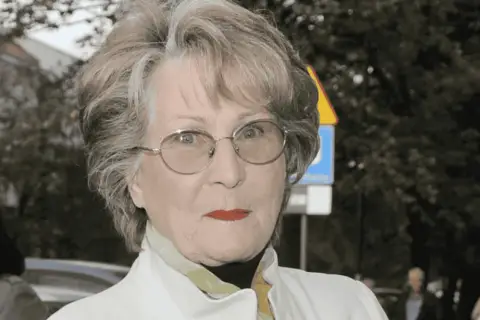Irena Santor w okularach, z czerwoną szminką na ustach, w białej kurtce. Myśli o swoich dzieciach.