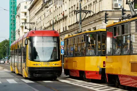 Dwa żółto-czerwone tramwaje stoją na ulicy, jeden z nich ma pierwszeństwo.