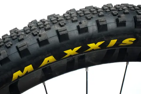 Close-up of a Maxxis Minion SS tire, showing its aggressive tread pattern and yellow branding. Ready for any trail.
