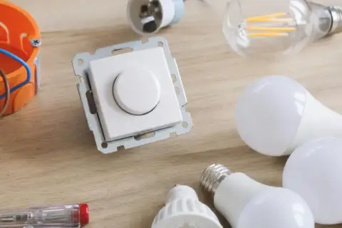 Ściemnianie led: biały ściemniacz, żarówki led, puszka instalacyjna i śrubokręt na drewnianym blacie.