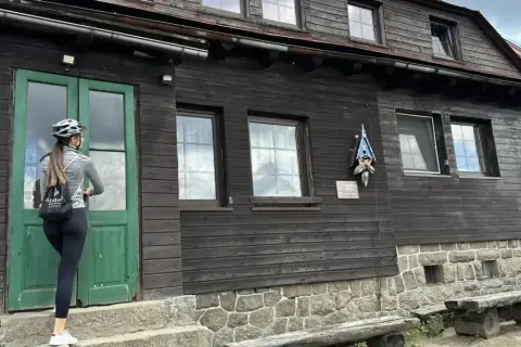 Kobieta w kasku rowerowym zbliża się do drzwi schroniska Chatka Górzystów.