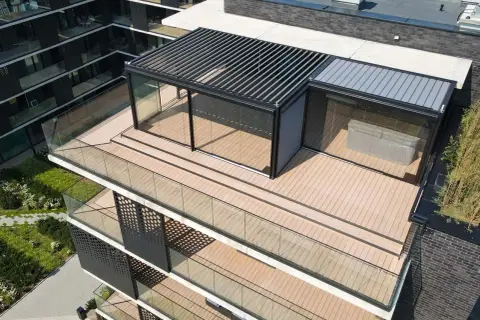 Nowoczesny taras na dachu z przeszklonym pawilonem i pergolą. Drewniana podłoga i szklane balustrady tworzą elegancką przestrzeń.