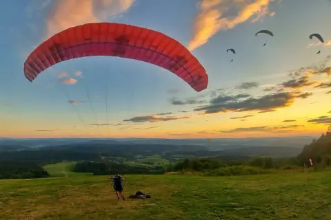 Szybowisko w Bezmiechowej o zachodzie słońca. Kilku paralotniarzy szybuje nad malowniczym krajobrazem.
