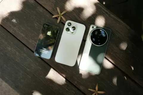 Trzy smartfony fotograficzne: stary iPhone, biały iPhone i zielony Huawei z aparatem Leica, leżą na drewnianym stole.