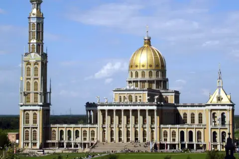 Bazylika w Licheniu z wysoką wieżą i złotą kopułą na tle błękitnego nieba.