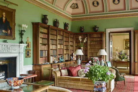 A cozy library with floor-to-ceiling bookshelves, a fireplace, and plush seating, embodying a classic countryside style.