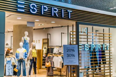 Sklep Esprit z neonowym logo. Manekiny prezentują letnie ubrania, a obok widoczna jest tablica z promocją.