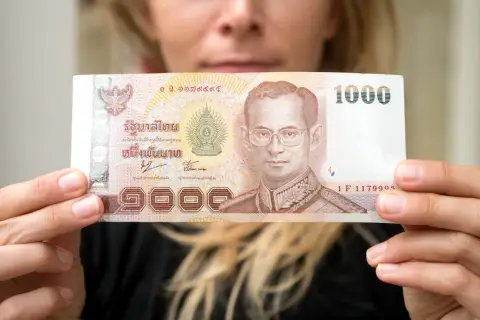 Kobieta trzyma banknot 1000 bahtów, co może pomóc w oszacowaniu, ile kosztuje życie w Tajlandii.