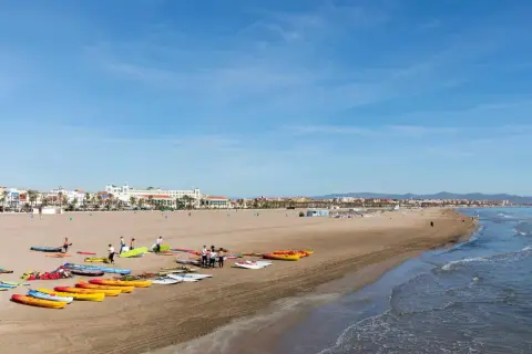 Gente prepara kayaks y tablas en la playa Malvarrosa, lista para un día de sol y mar.