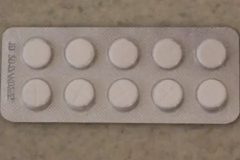 Opakowanie z dziesięcioma białymi tabletkami, niektóre z nacięciem. Może to być lek na receptę, np. tizagelan.