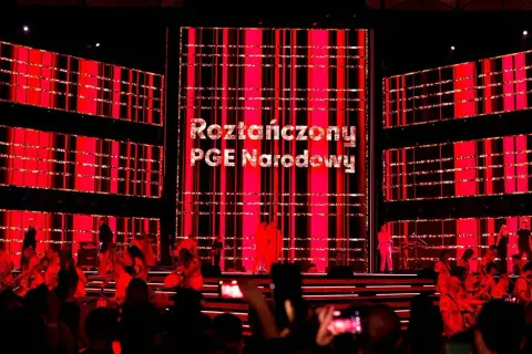 Roztańczony PGE Narodowy rozświetlony czerwienią. Na scenie artyści, w tle wielkie ekrany z napisem.