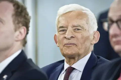 Jerzy Buzek, w otoczeniu innych mężczyzn, z uwagą słucha przemówienia.