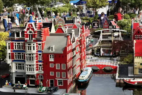Miniaturowa holenderska zabudowa z kanałami i mostami w **Lego Land**. Ludzie spacerują wśród kolorowych budynków z klocków.