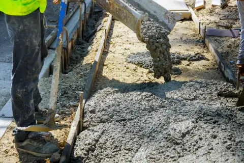 Betoniarka wylewa beton na plac budowy. Pracownik w kamizelce i spodniach przygotowuje teren. Zastanawiasz się, ile kosztuje kubik betonu?