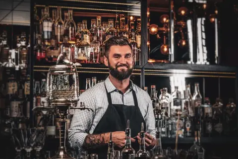Barman z tatuażami prezentuje akcesoria do przygotowania absyntu. Poznaj tajniki, jak pić absynt, by w pełni docenić jego smak.