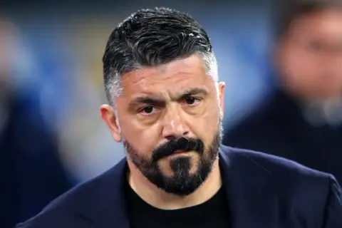 Gennaro Gattuso, zamyślony trener w granatowej marynarce, z charakterystyczną brodą i siwiejącymi włosami.