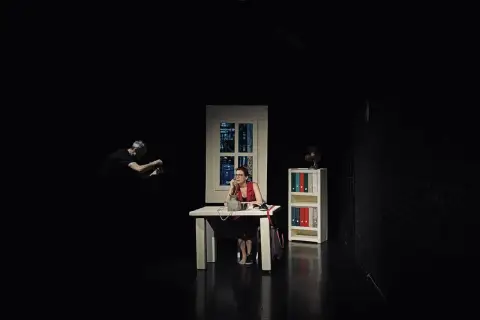 Scena w **teatrze Kana Szczecin**: kobieta przy biurku rozmawia przez telefon, mężczyzna w tle filmuje.
