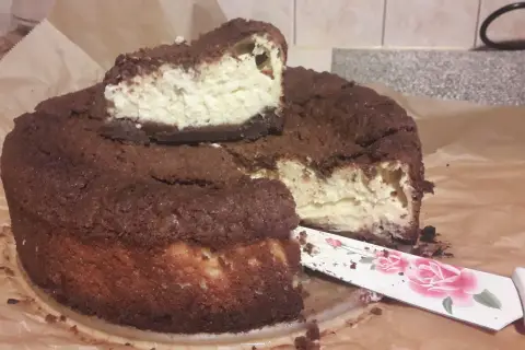 Pyszny sernik królewski bezglutenowy z czekoladową kruszonką i kremowym nadzieniem. Pokrojony kawałek czeka na spróbowanie.