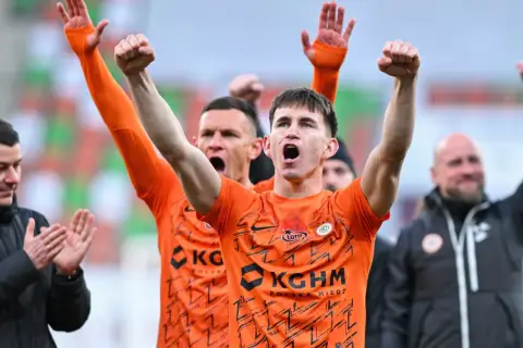 Marcel Reguła świętuje z drużyną, wznosząc ręce w geście radości.