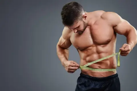 Mężczyzna z wyrzeźbionym brzuchem mierzy talię centymetrem, kontrolując efekty lean bulk.