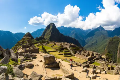 Machu Picchu, dawna twierdza Inków, wznosi się wśród zielonych gór. Turyści zwiedzają ruiny, podziwiając dzieło Inków.