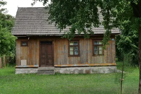Drewniany dom z gontowym dachem, otoczony zielenią. Widać tu, kiedy dom jest zabytkiem, z jego wiekową, ale wciąż piękną fasadą.