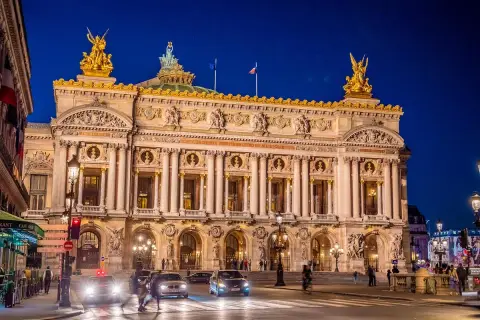 Słynny teatr w Paryżu, Opera Garnier, lśni w nocnym świetle. Złote rzeźby i bogata fasada zapraszają na wieczór pełen wrażeń.