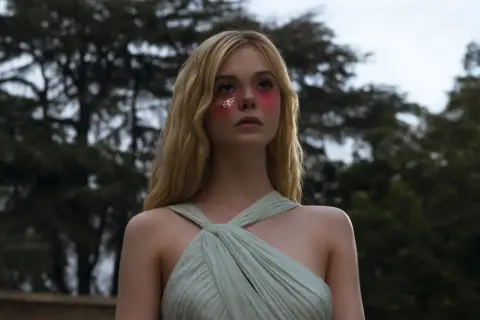 Ragazza con trucco glitterato e vestito verde pallido, un'immagine che evoca il significato di "The Neon Demon" e la sua ossessione per la bellezza.