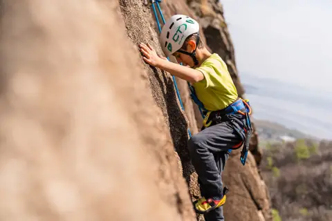Bambino con casco e imbracatura si arrampica su una parete rocciosa. Un'avventura di arrampicata per bambini, anche se ne avesse 3 anni!
