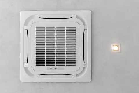 Kasetowa klimatyzacja zamontowana na suficie, obok kwadratowej lampy.