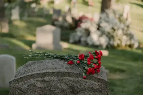 Un bouquet de fleurs rouges repose sur une pierre tombale dans un cimetière. Une question se pose : peut-on acheter une concession de son vivant ?