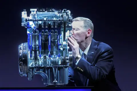 Mężczyzna w garniturze całuje silnik Forda. Wiele osób szuka **1.0 ecoboost opinie** przed zakupem.