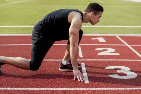 Mężczyzna w pozycji startowej na bieżni. Czy bieganie jest zdrowe? Ten sportowiec z pewnością tak uważa, gotowy do sprintu.
