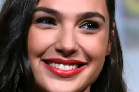 Zbliżenie na twarz Gal Gadot z szerokim uśmiechem i czerwonymi ustami.