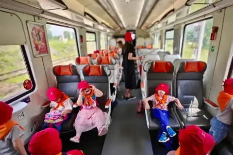 Dzieci w czerwonych kapeluszach podróżują pociągiem. Czy w Polregio jest rezerwacja miejsc? Siedzenia są wygodne, a podróż zapowiada się ciekawie.