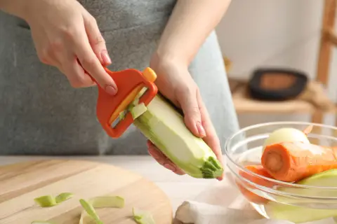 Ręce obierają cukinię obieraczką. Czy można jeść surową cukinię? Tak, po obraniu i pokrojeniu.