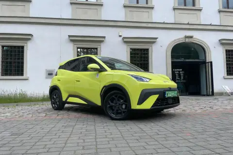Jaskrawożółty BYD Seagull zaparkowany na bruku przed budynkiem z łukowym wejściem.