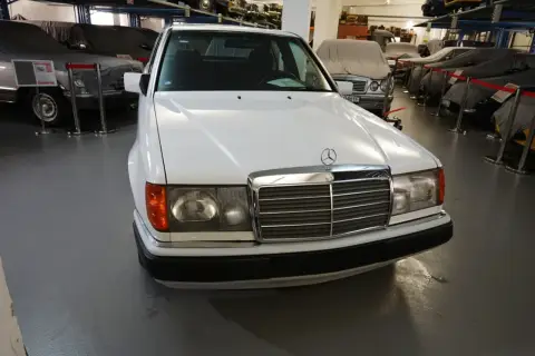 Biały Mercedes "Baleron" z lat 80. stoi w muzeum obok innych zakrytych samochodów.