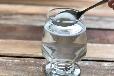 Łyżeczka z proszkiem, który może być naturalny kolagen na stawy, wsypywana do szklanki z wodą.