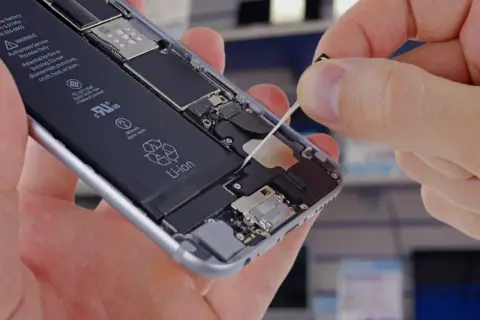 Wymiana baterii w iPhone. Dłoń wyciąga taśmę z wnętrza telefonu, odsłaniając baterię Li-ion.